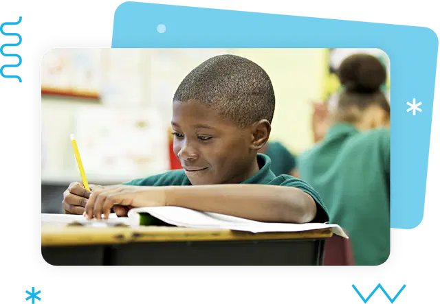 A child in a green shirt smiles while writing in a notebook at a classroom desk, engaged in their k–5 literacy curriculum, with another student visible in the background.