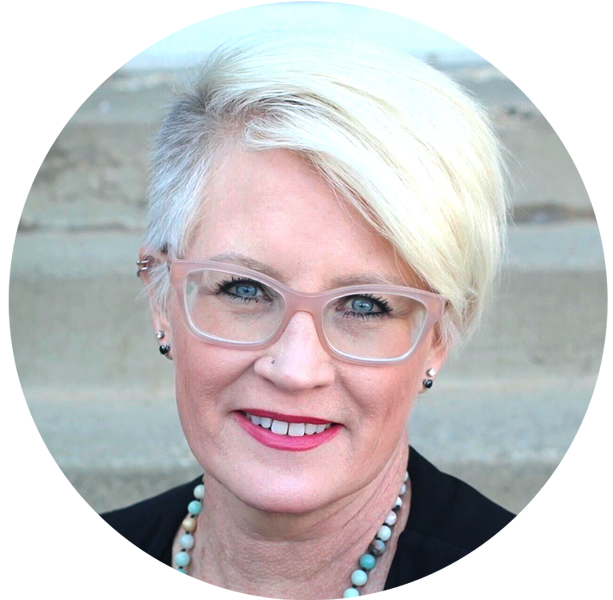 Retrato de una mujer caucásica sonriente con cabello rubio corto, involucrada en un podcast sobre la ciencia de la lectura, con gafas, lápiz labial rojo y un collar de perlas.