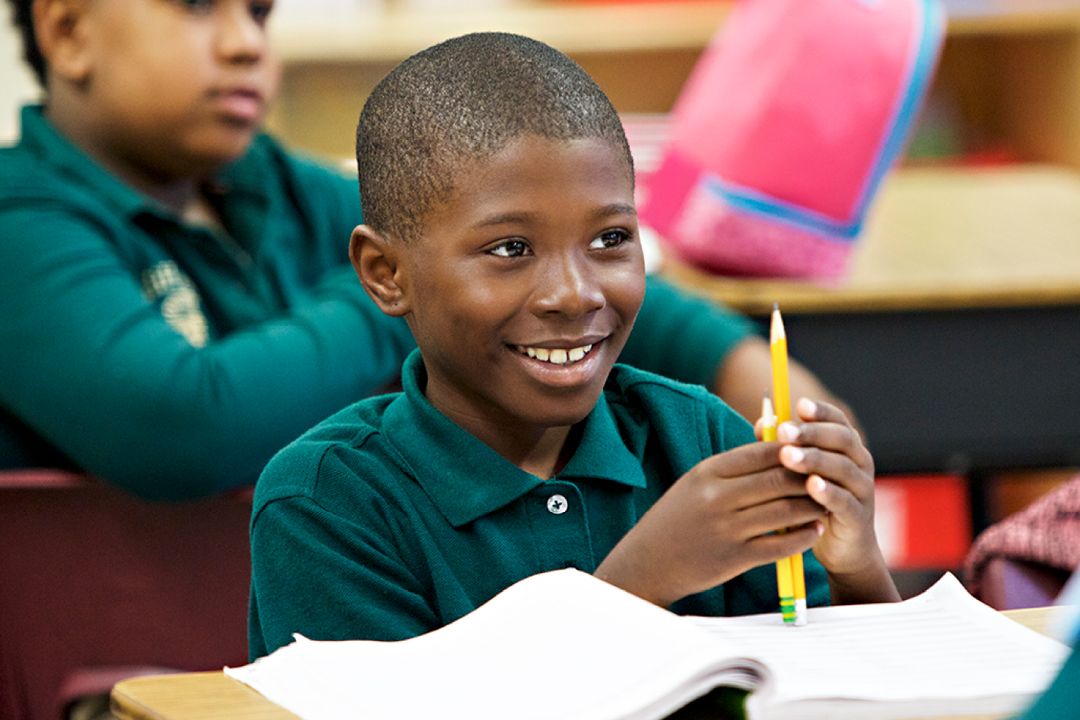 The boy smiles and holds a pencil in his hands