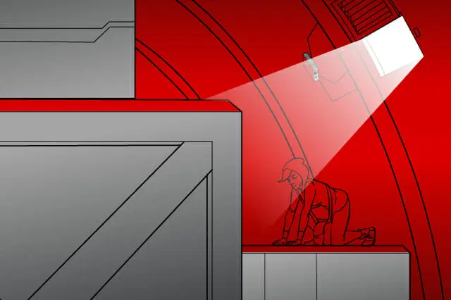 Una persona con sombrero y ropa informal se arrastra en una habitación roja con poca luz, iluminada por un solo foco. En primer plano aparecen varios objetos geométricos de gran tamaño.