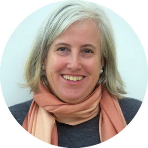 A smiling person with shoulder-length gray hair, wearing a peach-colored scarf and a gray sweater, stands against a plain white background. This image captures the essence of Pennsylvania teachers who are dedicated to enriching Science programs for elementary students.