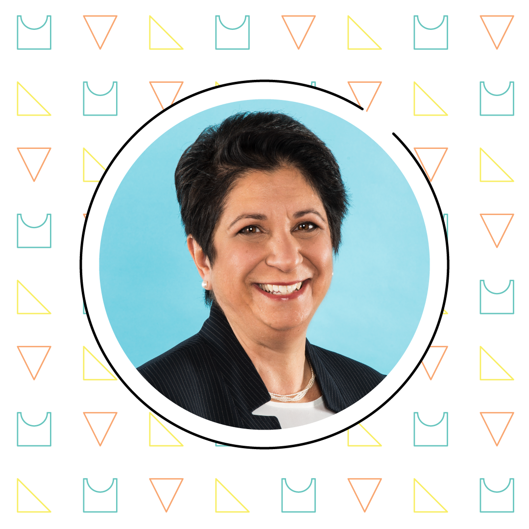 Portrait of a smiling woman with short hair, wearing a suit, set against a blue background within a white circular frame on a patterned turquoise and black background that subtly incorporates sesame workshop themes.