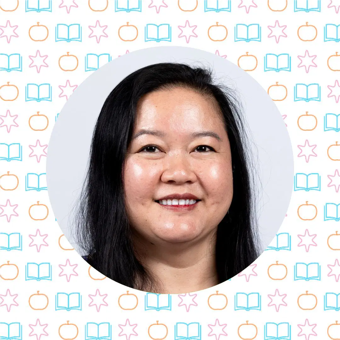 Una mujer con cabello largo y oscuro sonríe a la cámara sobre un fondo con patrones repetidos de manzanas, estrellas y libros.