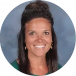 A woman with long dark hair smiles in front of a plain background, reflecting the joy she finds in interdisciplinary research. She is wearing a dark green top and earrings.