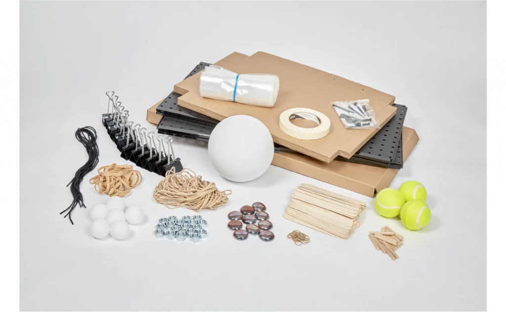 On a white background are various supplies, such as cardboard sheets, pegboards, hooks, rubber bands, tennis balls, popsicle sticks, tape, and other small objects.