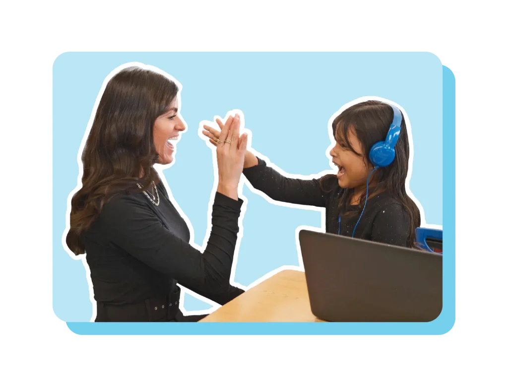 An adult and a child wearing blue headphones joyfully high-five each other at a table with a laptop, celebrating their success with an engaging tutoring program.