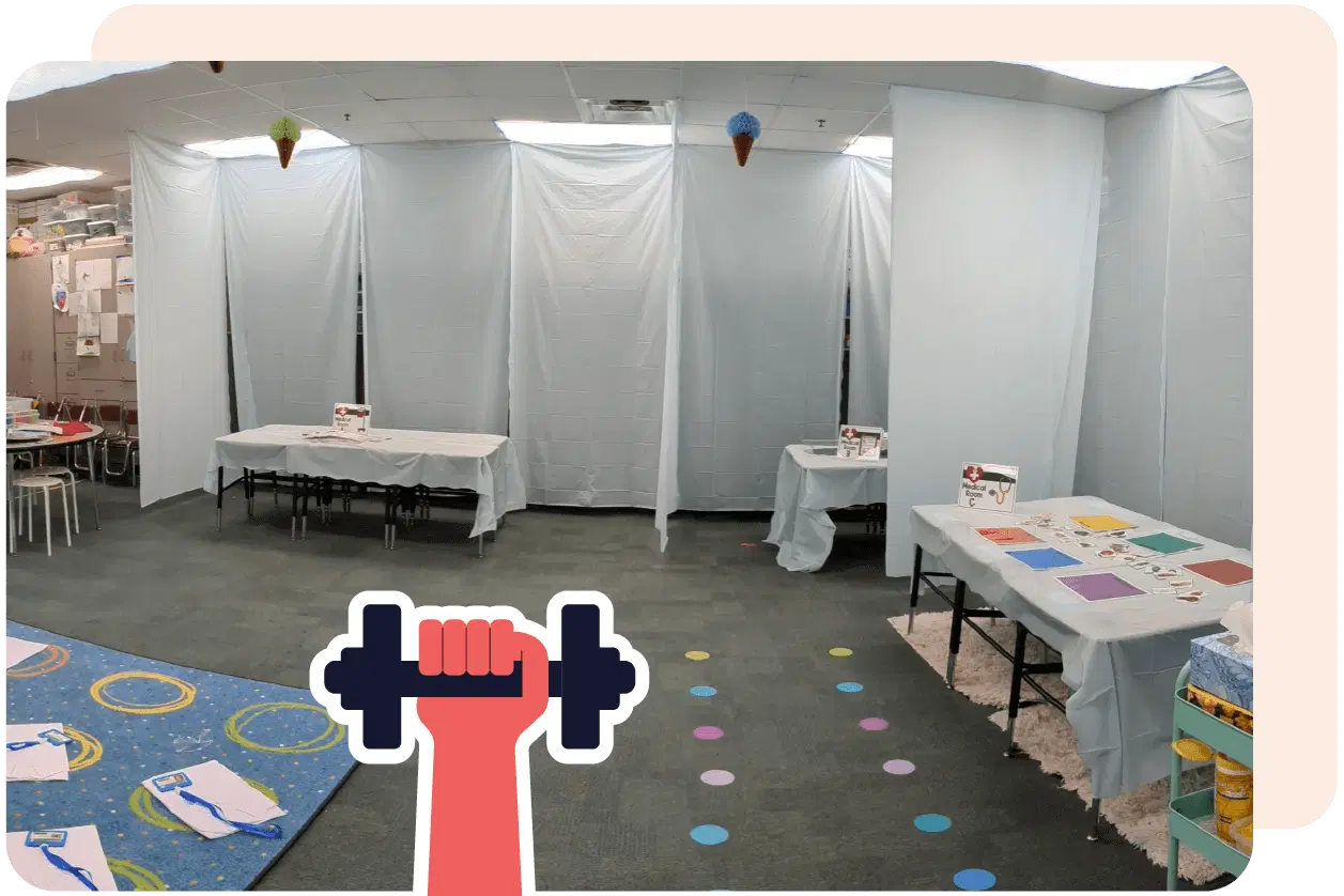 Classroom with light blue walls and ceiling, tables covered with white cloth, and colorful worksheets. A cartoon hand holding a dumbbell is overlaid on the image.