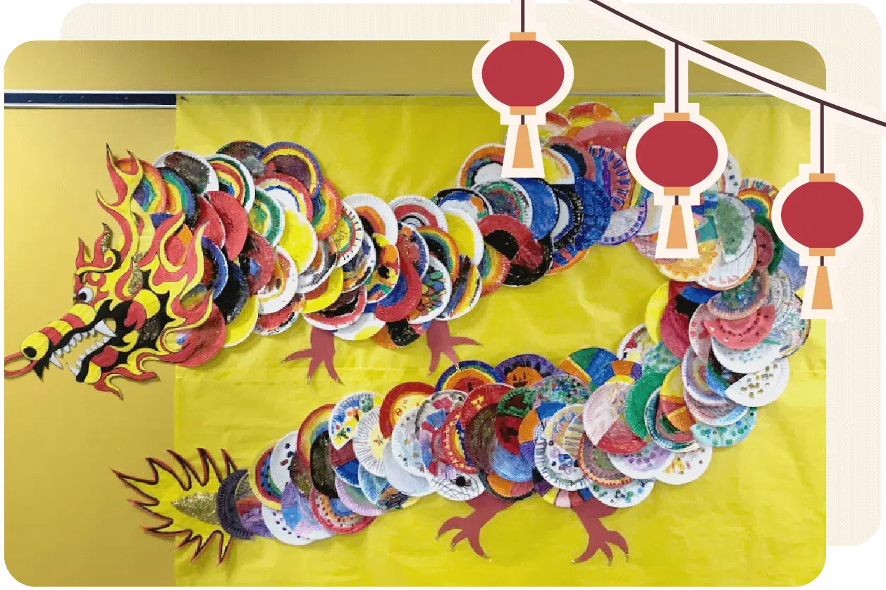 Colorful dragon made of decorated paper plates on a yellow background, with red lanterns hanging above.