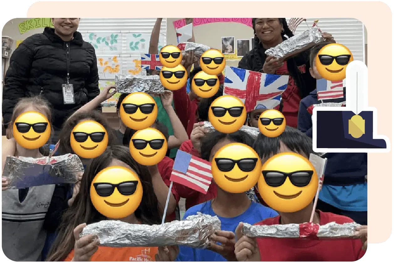 Children hold aluminum foil ships and various flags, with smiling face emojis covering their faces. Adults stand in the background.