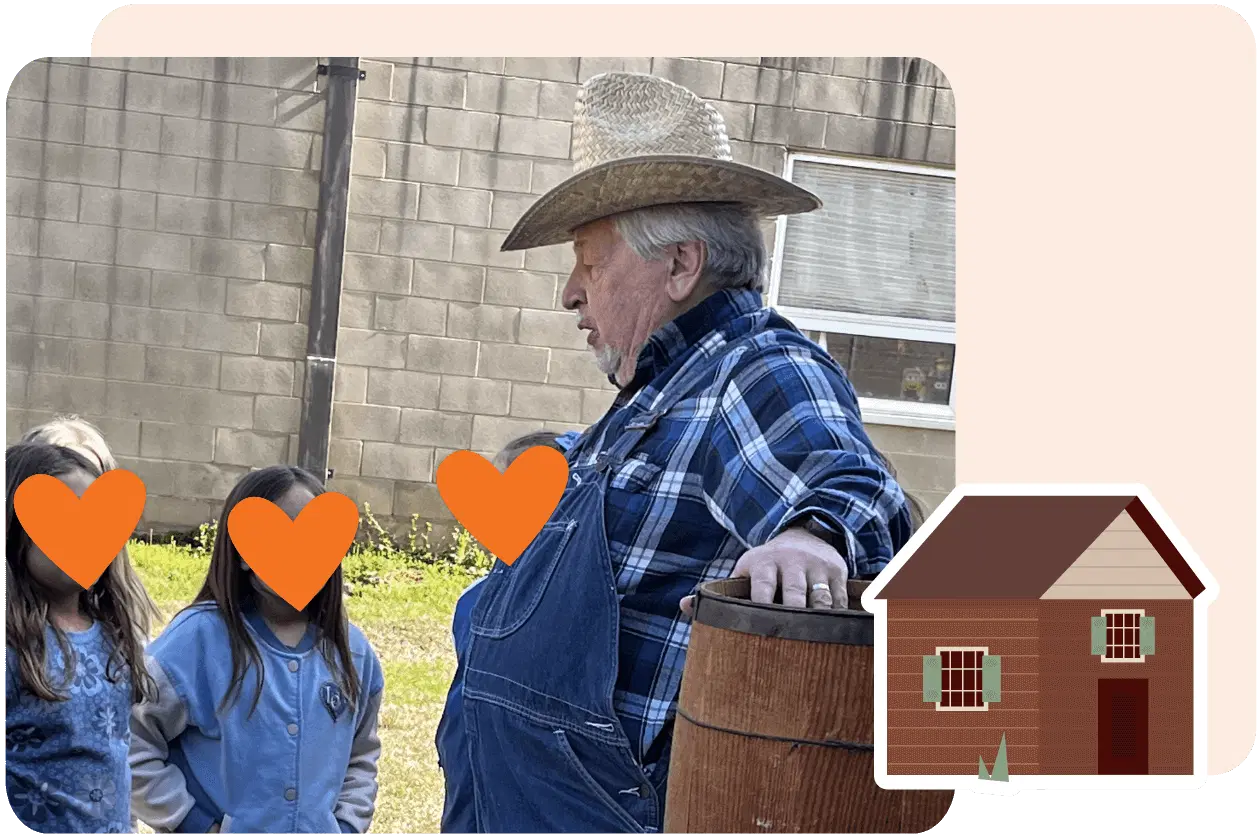 A man in a straw hat and overalls talks to children outdoors, standing beside a barrel.