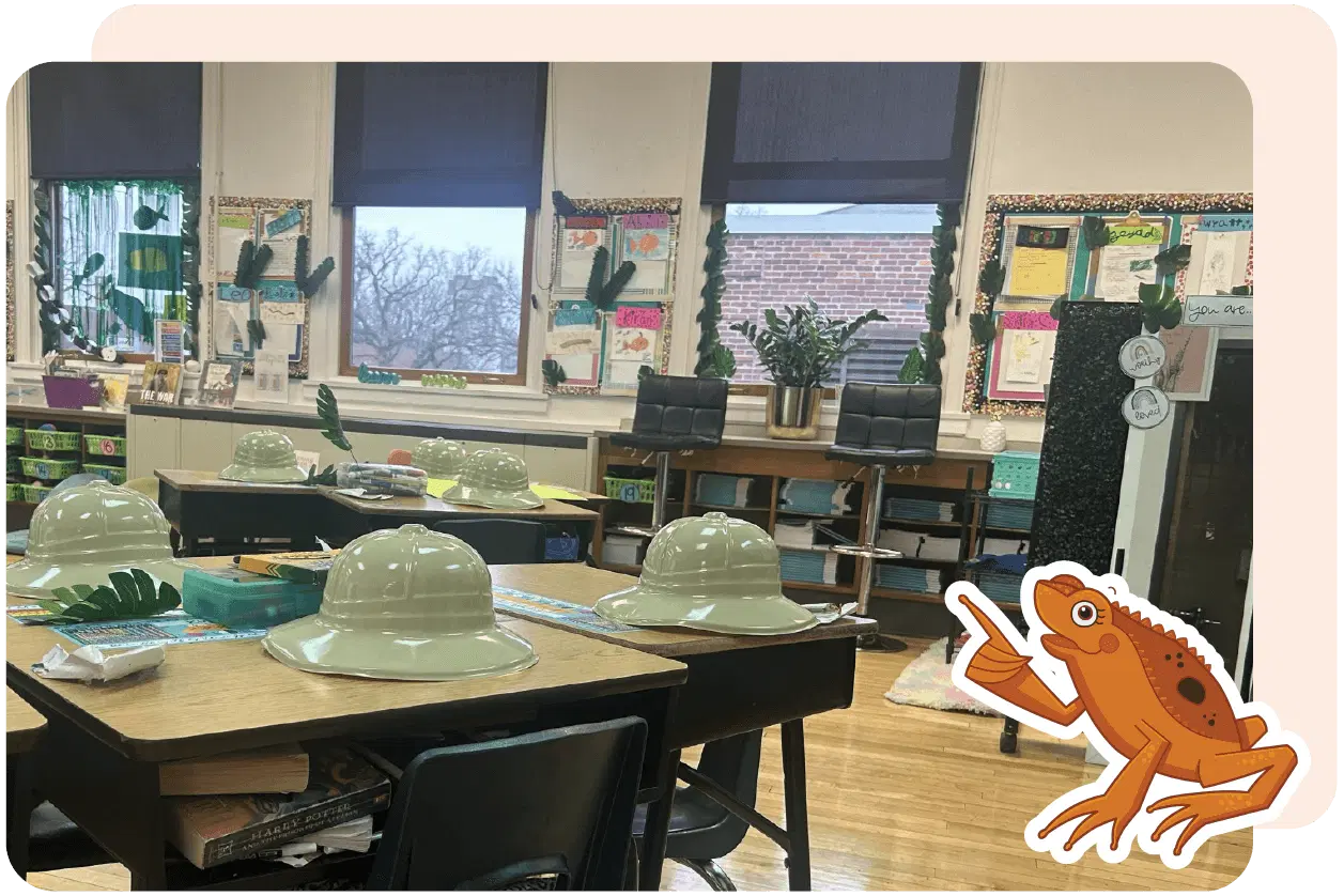 Classroom with desks arranged in groups. Pith helmets on tables, plant-themed decor, and a cartoon frog with a pointer on the wall. Large windows with blinds.