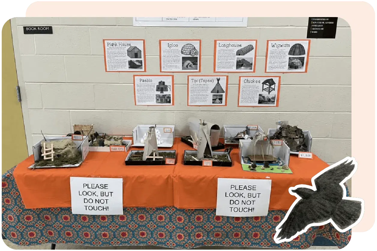 Table display of various architectural models with educational signs on a patterned tablecloth. Wall behind shows information sheets. Signs read: "PLEASE LOOK, BUT DO NOT TOUCH!" Bird silhouette overlay.