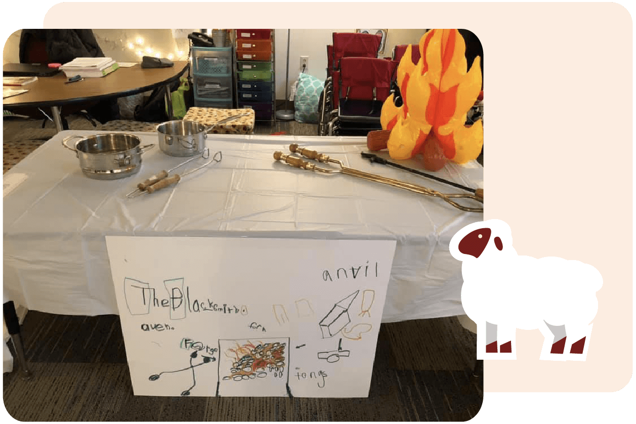 A table with brass instruments and a plush flame decoration. A hand-drawn sign with the text "The Blacksmith" and various drawings is displayed in front.