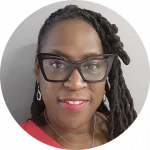 A person with long braided hair, wearing oversized glasses, earrings, a necklace, and a red top, smiles at the camera against a plain background.
