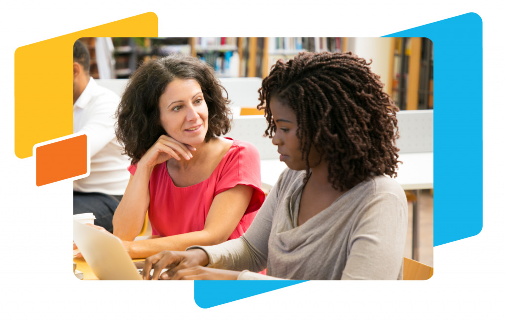 Two women seated at a table engage in a lively conversation. One is using a laptop, likely discussing innovative teaching practices. Bookshelves filled with resources for empowering students are visible in the background, perhaps hinting at their dedication to star awards in education.