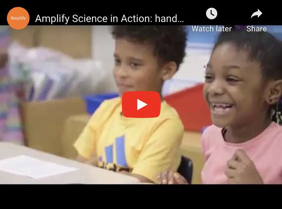 Two children sitting at a table, one in a yellow shirt and the other in pink, smiling and looking forward.