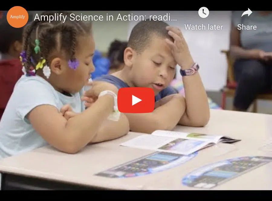 Two young children sit at a table looking at an open book, with other books placed in front of them. A play button is visible over the image.