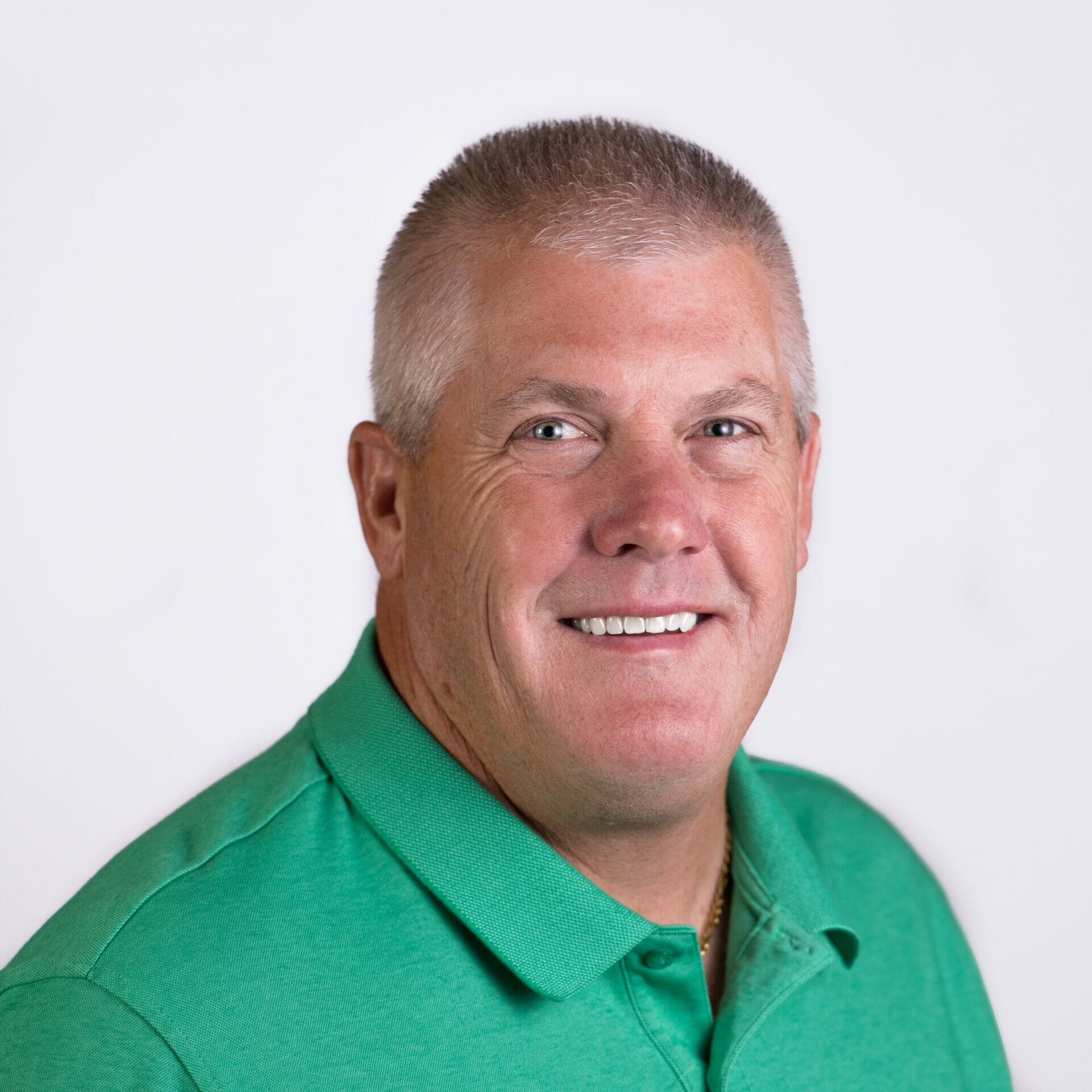 A person with short gray hair smiles at the camera, wearing a green collared shirt against a plain background.