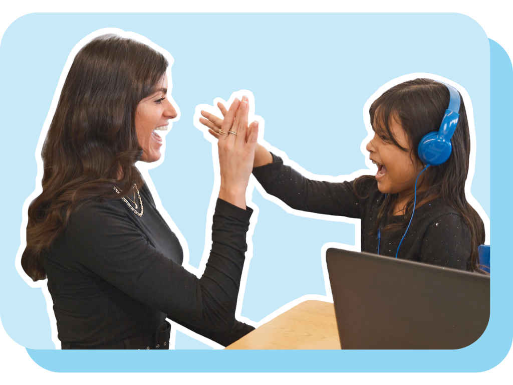An adult and a child wearing headphones smiling and high-fiving each other at a desk with a laptop.