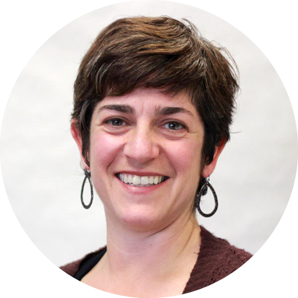A woman with short brown hair, wearing hoop earrings and a maroon top, smiles at the camera against a plain light background, radiating confidence and passion for math and science.