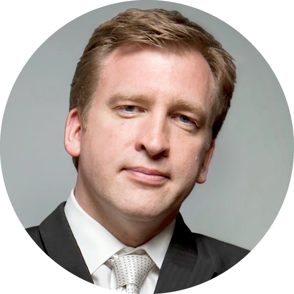 A man in a suit and tie with short light brown hair, light skin, and a neutral expression, posed against a plain background—his demeanor suggesting a professional in math and science.