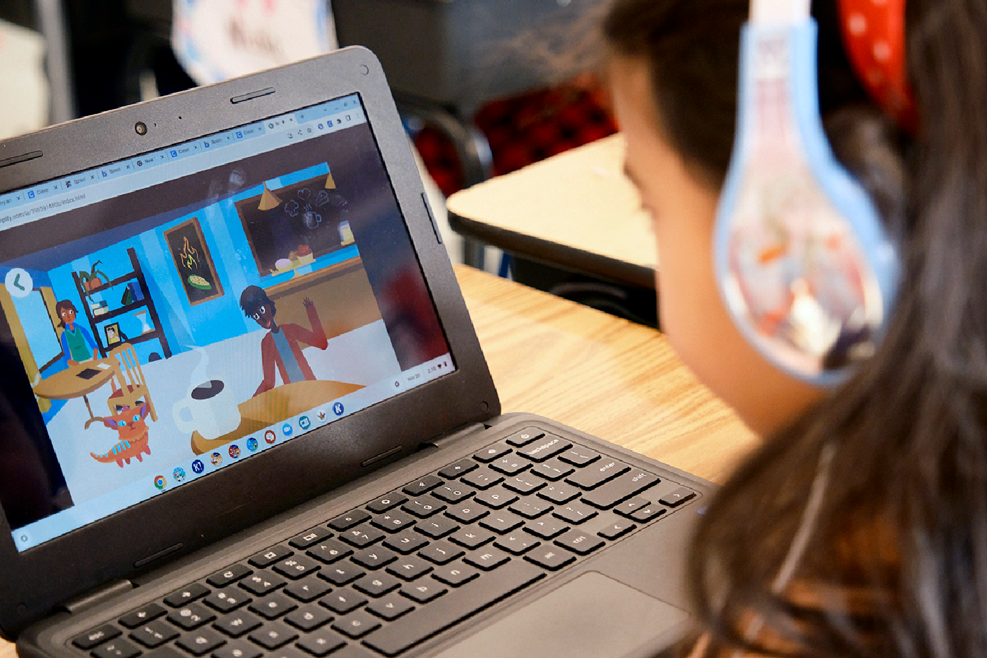 A child wearing headphones sits at a desk using a laptop, which displays a colorful animated video with cartoon characters in a room to ayudar a ampliar el plan de estudios.
