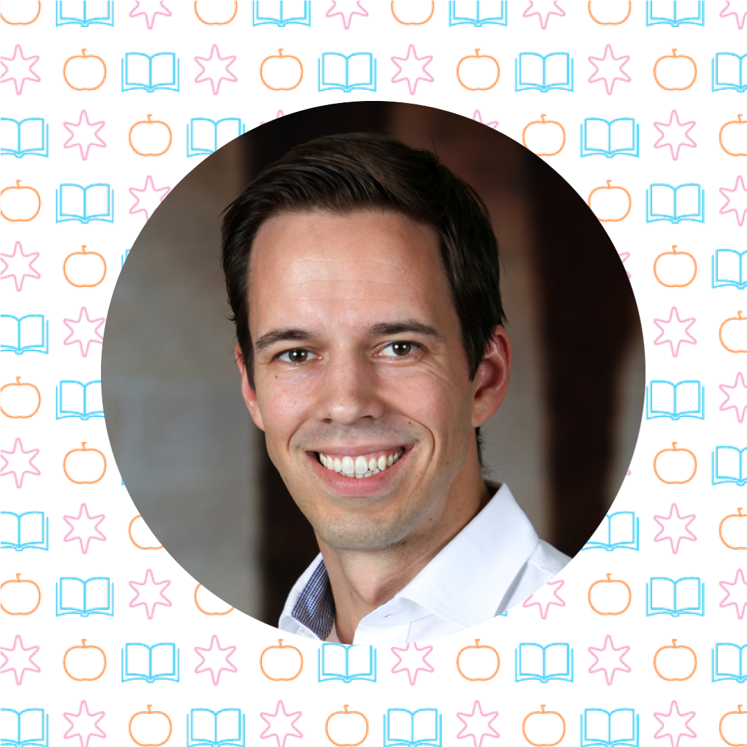 A man with short dark hair smiles at the camera. The background is a circular frame over a patterned backdrop featuring books, stars, and apples—perfect for sharing tips for teachers in a joyful classroom setting.