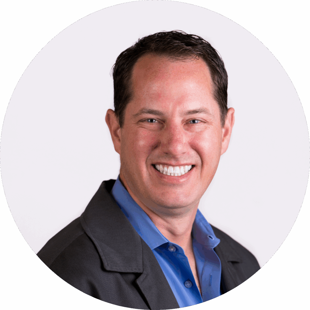 A smiling man in a grey blazer and blue shirt, against a white background.