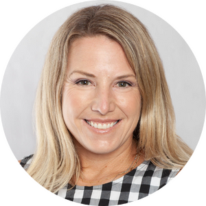 A woman with long blonde hair, wearing a black and white checkered top, smiling in front of a plain light background.