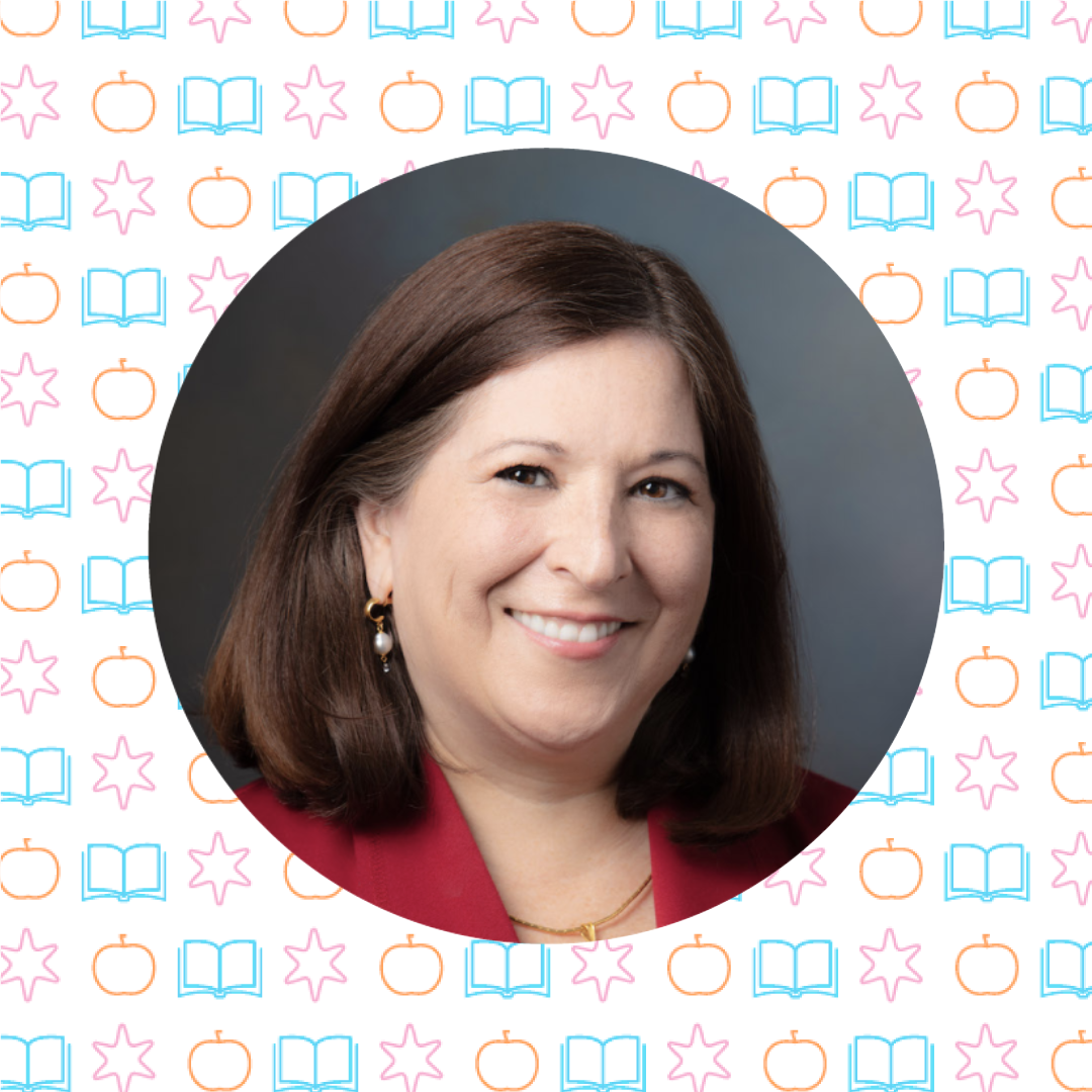 A woman with straight brown hair smiles at the camera, wearing a red blazer and pearl earrings, set against a patterned background of books, apples, stars, and math instruction symbols.