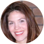 A woman with shoulder-length brown hair smiles in front of a brick wall.