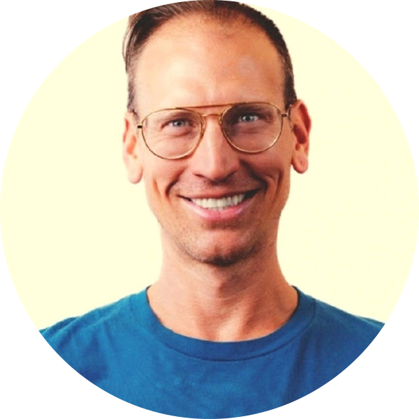 A man with short brown hair, glasses, and a blue shirt smiles at the camera against a light background.