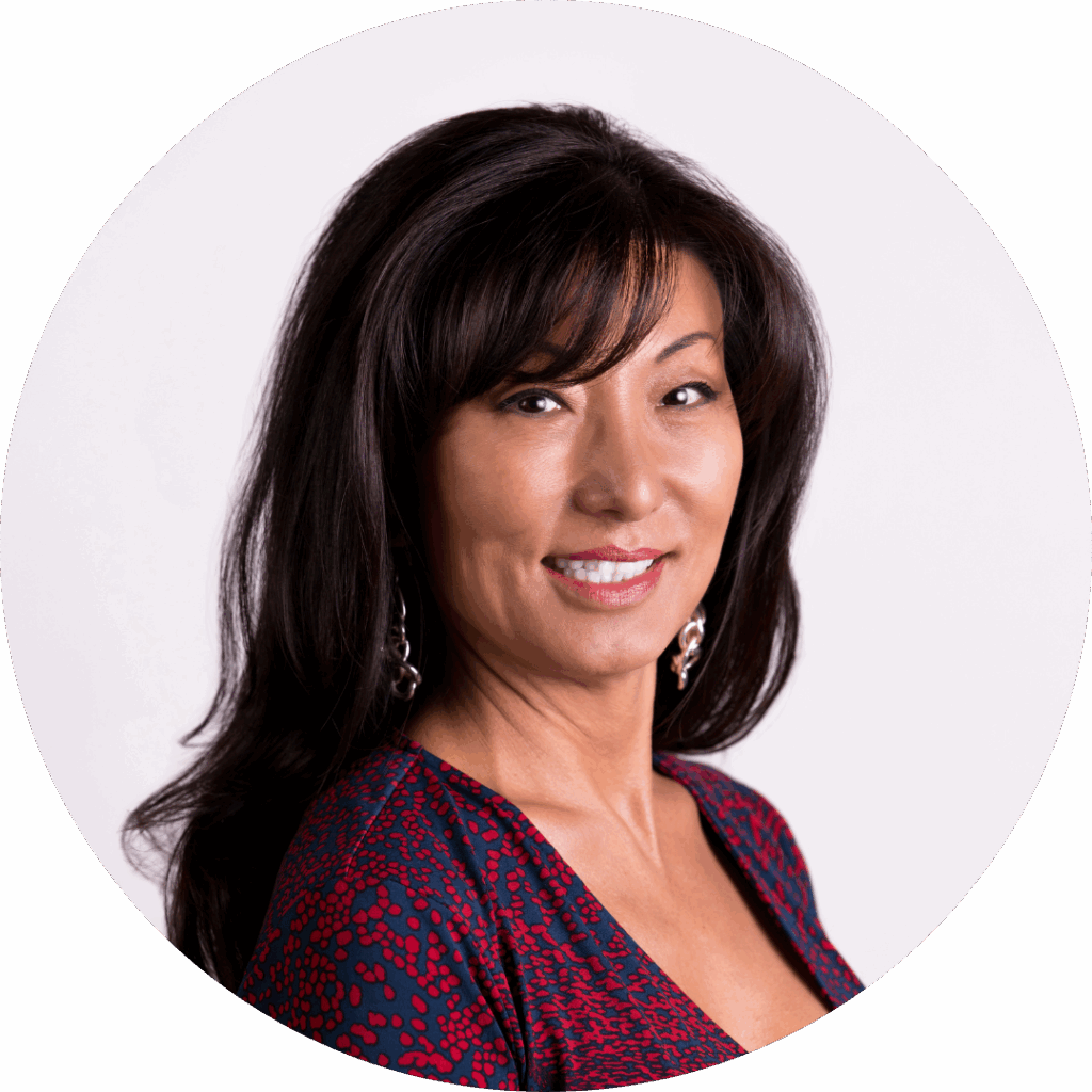 A professional headshot of a middle-aged asian woman with shoulder-length black hair, wearing a red and black patterned top and earrings, smiling against a white background.