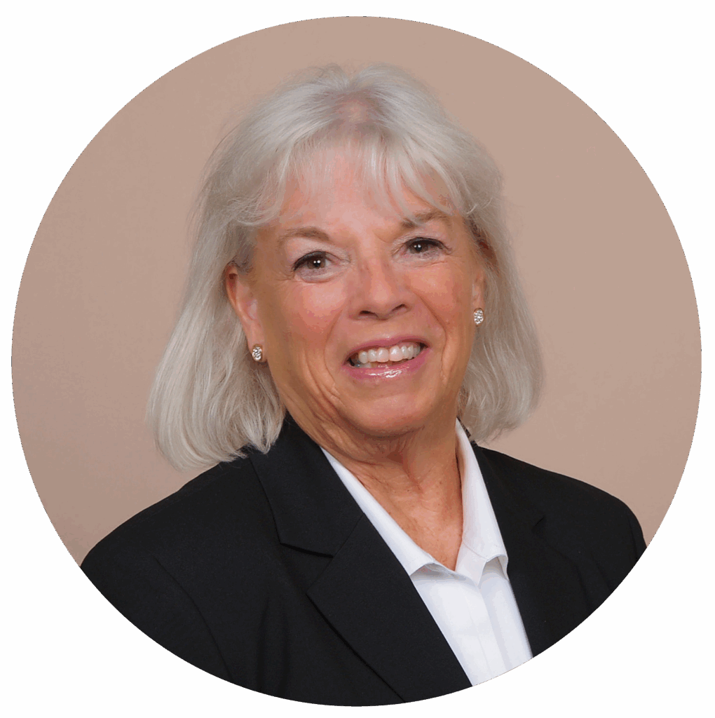 Elderly woman with white hair smiling, wearing a black blazer and white blouse against a soft beige background.