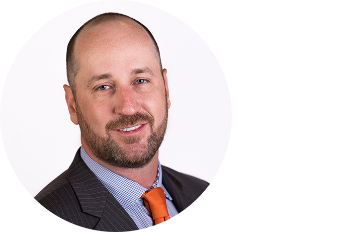A man with a beard and short hair, wearing a striped suit, blue shirt, and orange tie, poses against a plain white background.