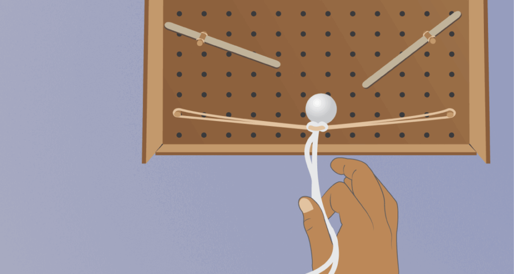 A hand pulls a white string attached to a pegboard with rubber bands and a white ball hanging from the center.