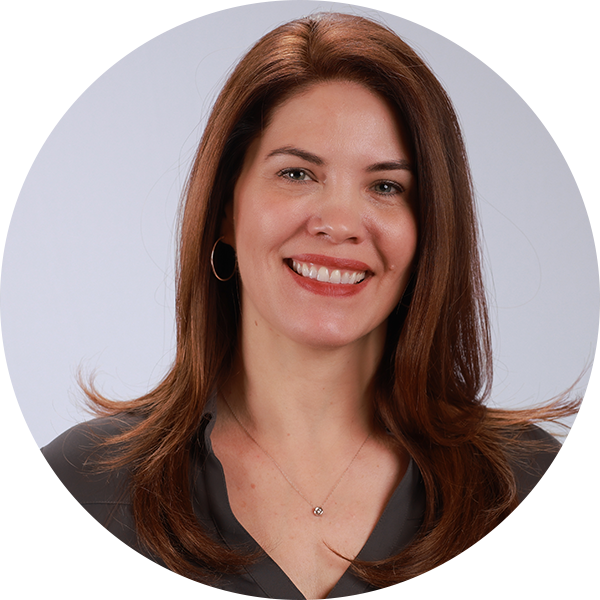 A woman with long brown hair, wearing a dark blouse and a necklace, smiles at the camera against a plain light background—an inspiring Indiana teacher recognized for her use of Amplify Science in the classroom.