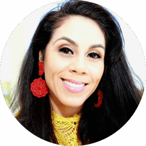 Woman with long dark hair, wearing red earrings and a yellow lace top, smiling at the camera against a light background—radiating the confidence of new teachers overcoming disillusionment in their journey.