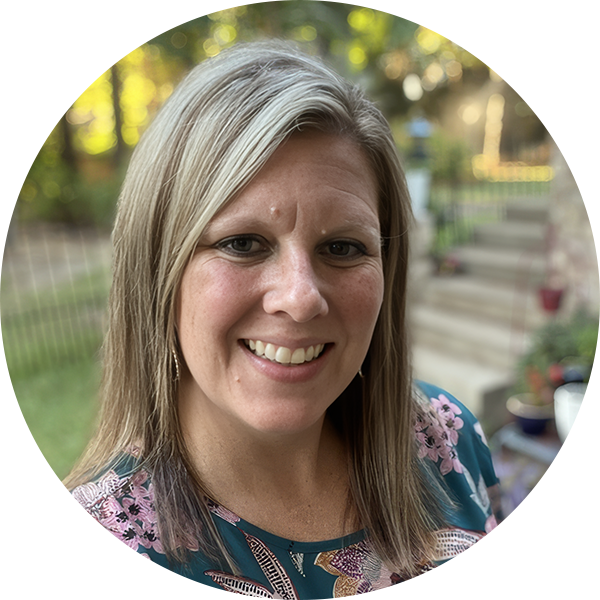 A woman with straight blonde hair smiles outdoors, standing in front of steps and greenery. She is wearing a patterned top.