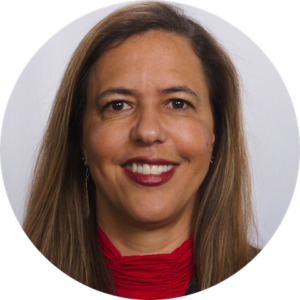 Portrait of a smiling woman with long brown hair, wearing a red top and earrings, set against a white background.