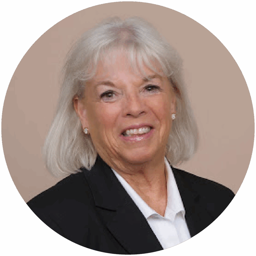 Portrait of a woman with white hair, smiling, wearing a black blazer against a light brown background.