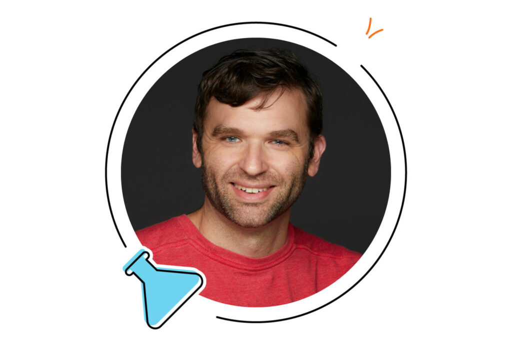 A man with short brown hair and a beard smiles at the camera, wearing a red shirt, framed by a circular graphic with a blue flask icon.